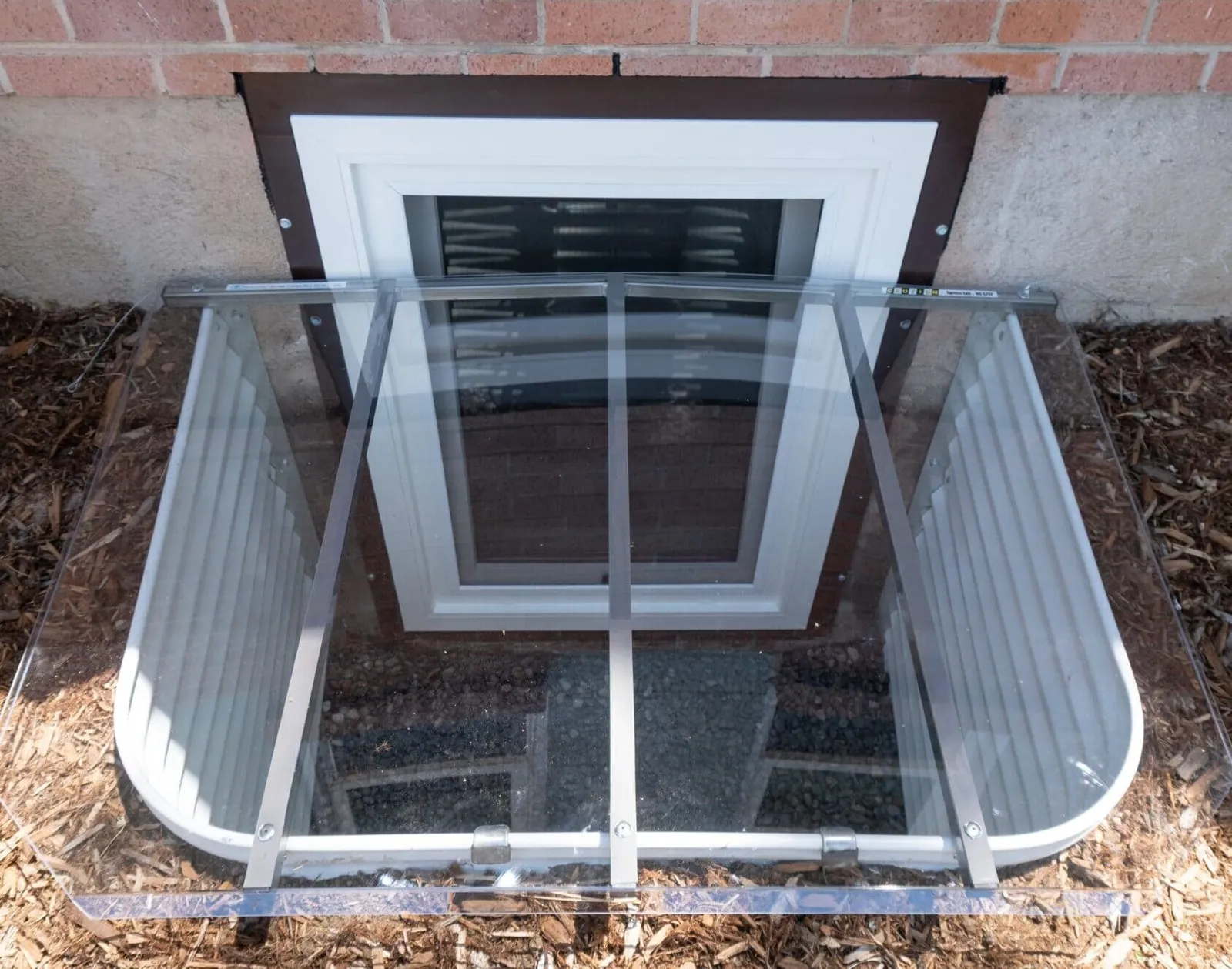 Egress window with a clear cover over a steel window well on a brick home
